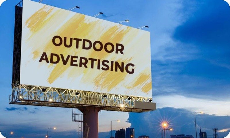 A large, eye-catching hoarding advertisement displayed on a busy Delhi street with vehicles and pedestrians passing by—demonstrating the high visibility and impact of outdoor billboard advertising.