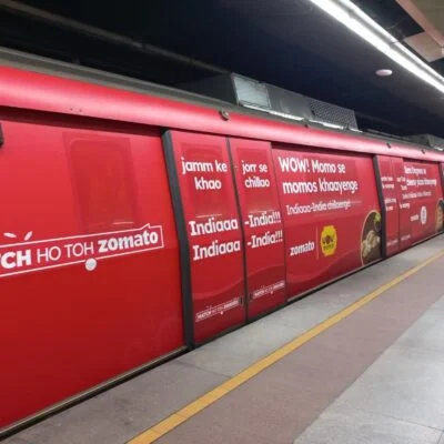 Zomato’s full metro train wrap branding with food slogans, executed by Acme Advertising Co. to target urban commuters at metro stations.